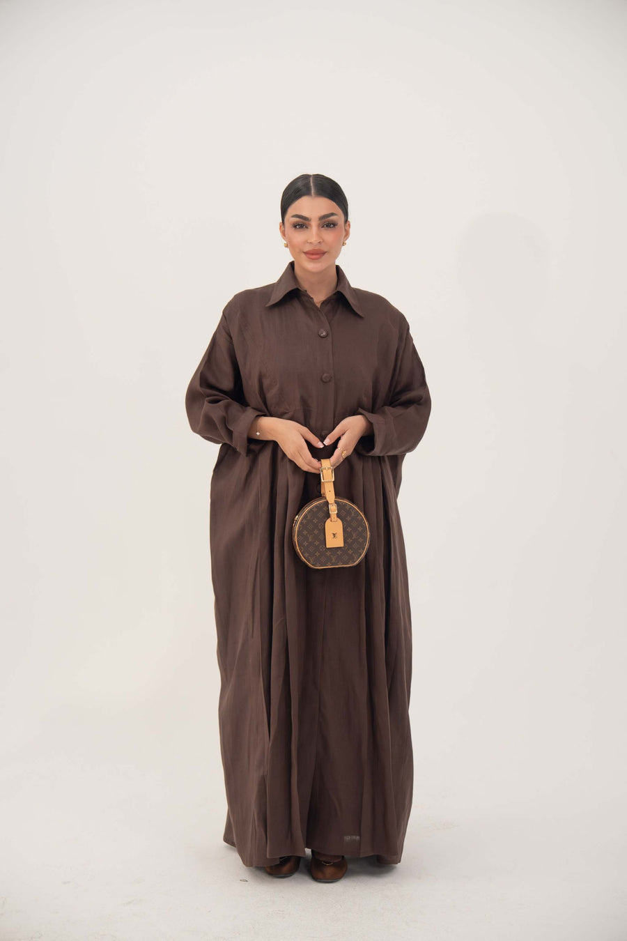 Woman wearing a deep cocoa brown linen shirt-style abaya with long sleeves and button-down front, holding a round brown handbag.