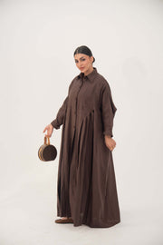 Woman wearing a deep cocoa brown linen shirt-inspired abaya with a flowy silhouette and tonal button-down front, holding a round handbag.