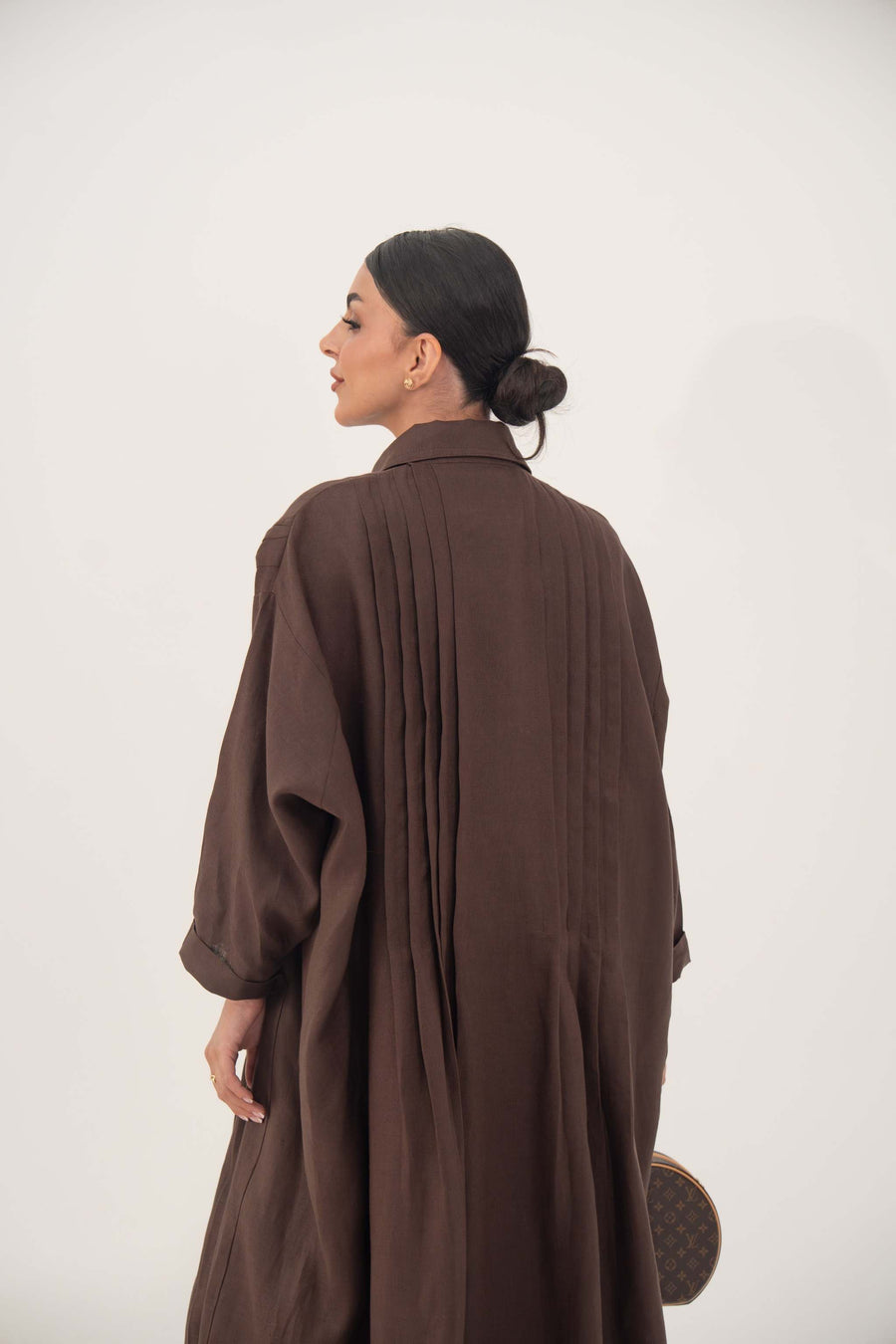 Back view of a woman wearing a deep cocoa brown, flowy linen abaya with a shirt collar and relaxed long sleeves