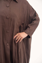 Close-up of a deep cocoa brown linen abaya with a shirt collar, tonal buttons, and relaxed long sleeves.