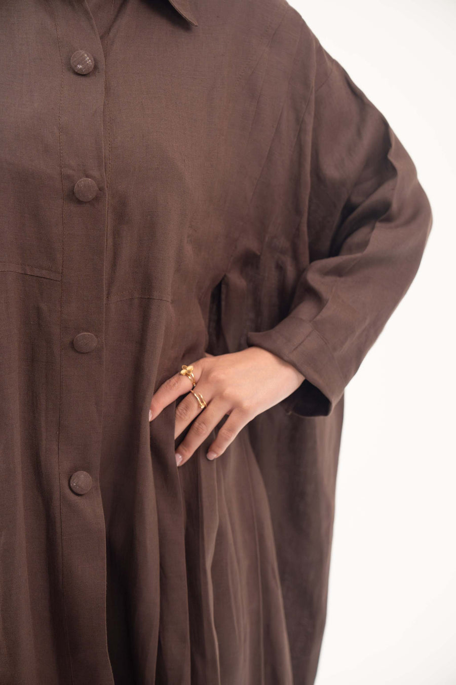 Close-up of a deep cocoa brown linen abaya with a shirt collar, tonal buttons, and relaxed long sleeves.
