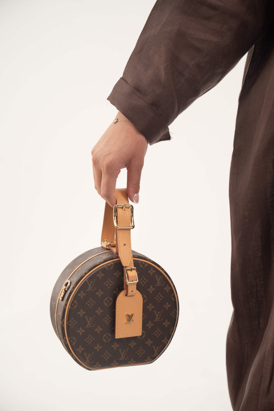 Hand holding round Louis Vuitton monogram handbag with brown linen Jupitor abaya sleeve visible