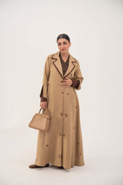 Dark brown A-line linen abaya with beige pleated panels and cream floral embroidery, featuring draped lapel and full lining for comfort.