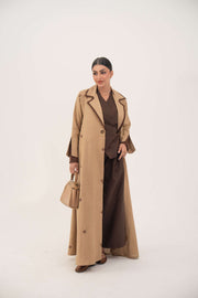 woman wearing cinnamon lightweight linen abaya with pleated side panels and floral embroidery carrying beige handbag