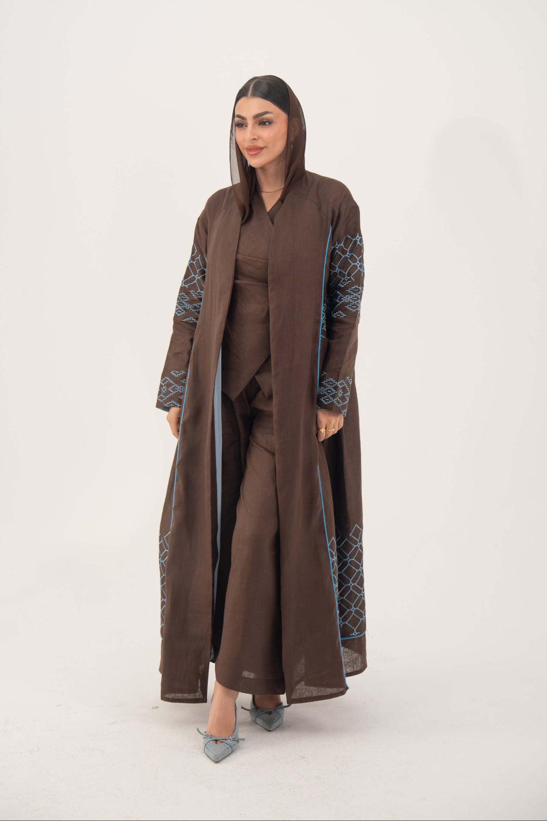 woman wearing rich mocha brown abaya with blue embroidery and piping, lightweight linen-blend fabric, open front, batwing cut, styled for warm weather