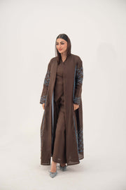 woman wearing rich mocha brown abaya with blue embroidery and piping, lightweight linen-blend fabric, open front, batwing cut, styled for warm weather