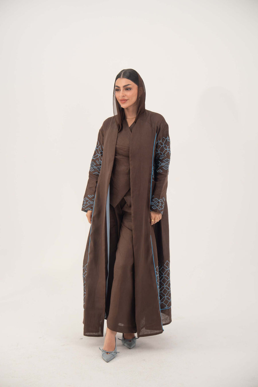 woman wearing rich mocha brown abaya with blue embroidery and piping, lightweight linen-blend fabric, open front, batwing cut, styled for warm weather