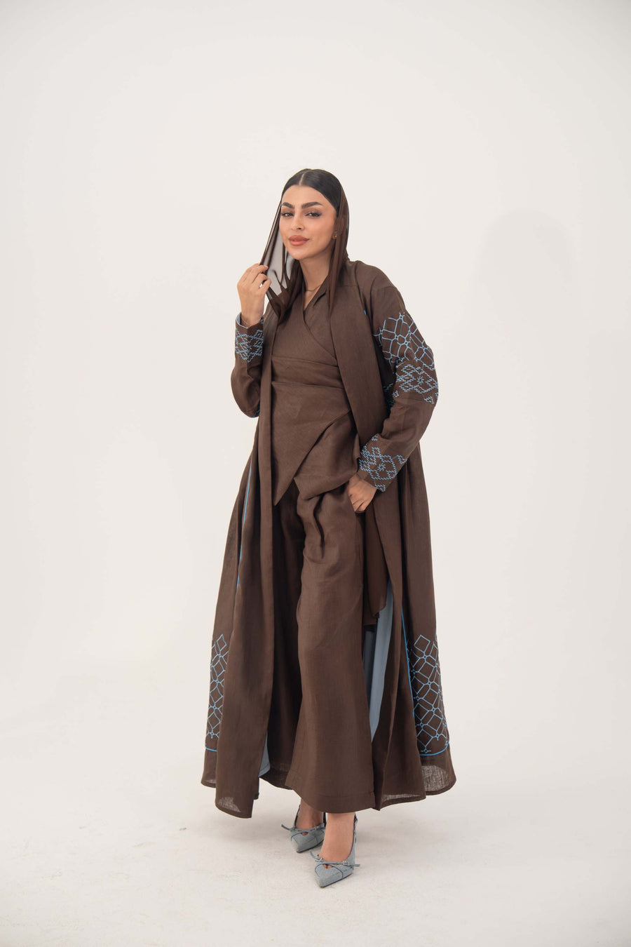 Mocha brown linen-blend abaya with sky-blue embroidery on sleeves and back, batwing cut, blue piping, open front, and light-blue inner cuffs.