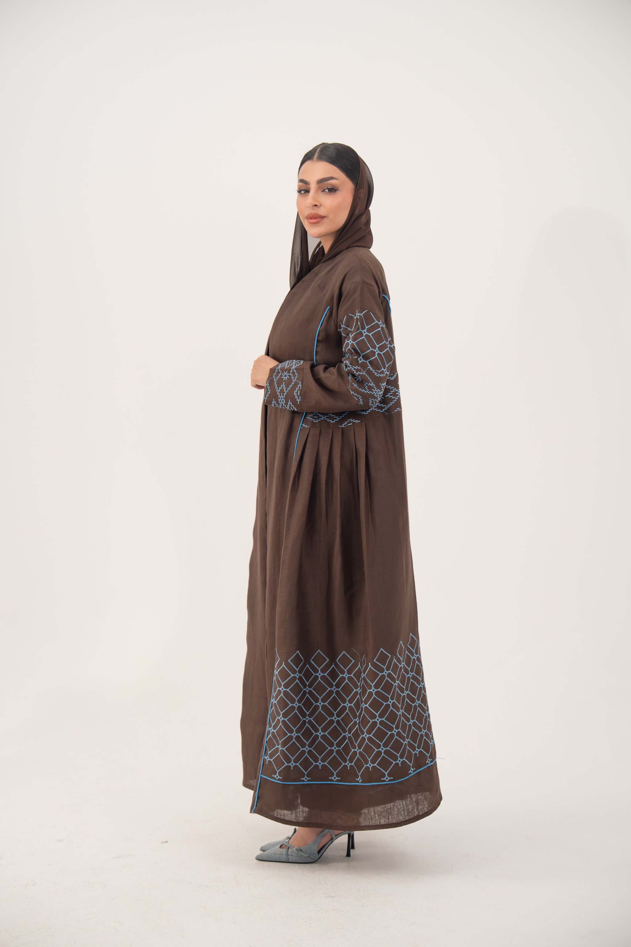 Mocha brown linen-blend abaya with blue embroidery panel on back and sleeves, batwing cut with blue piping, and light-blue cuff detail.