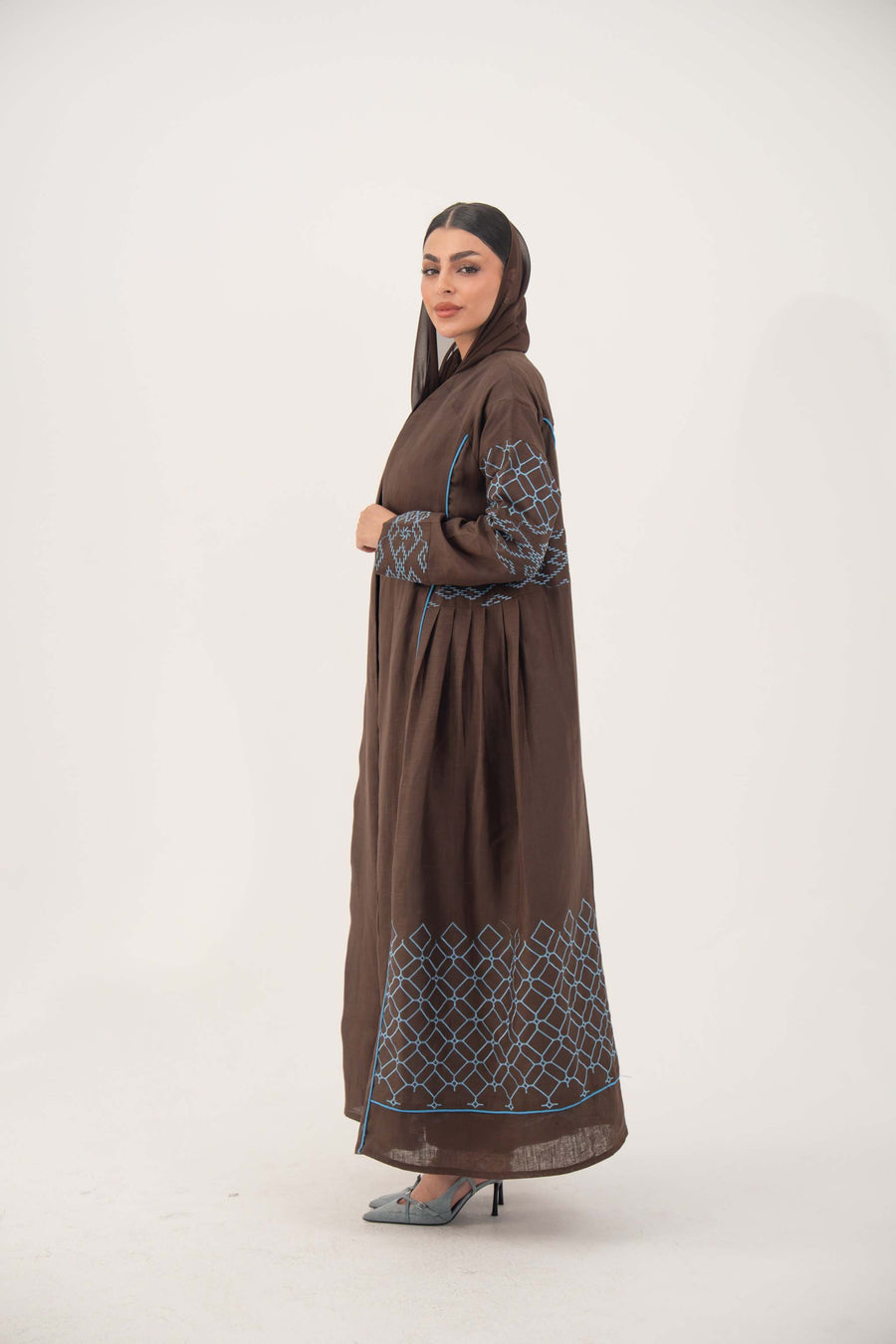 Mocha brown linen-blend abaya with blue embroidery panel on back and sleeves, batwing cut with blue piping, and light-blue cuff detail.