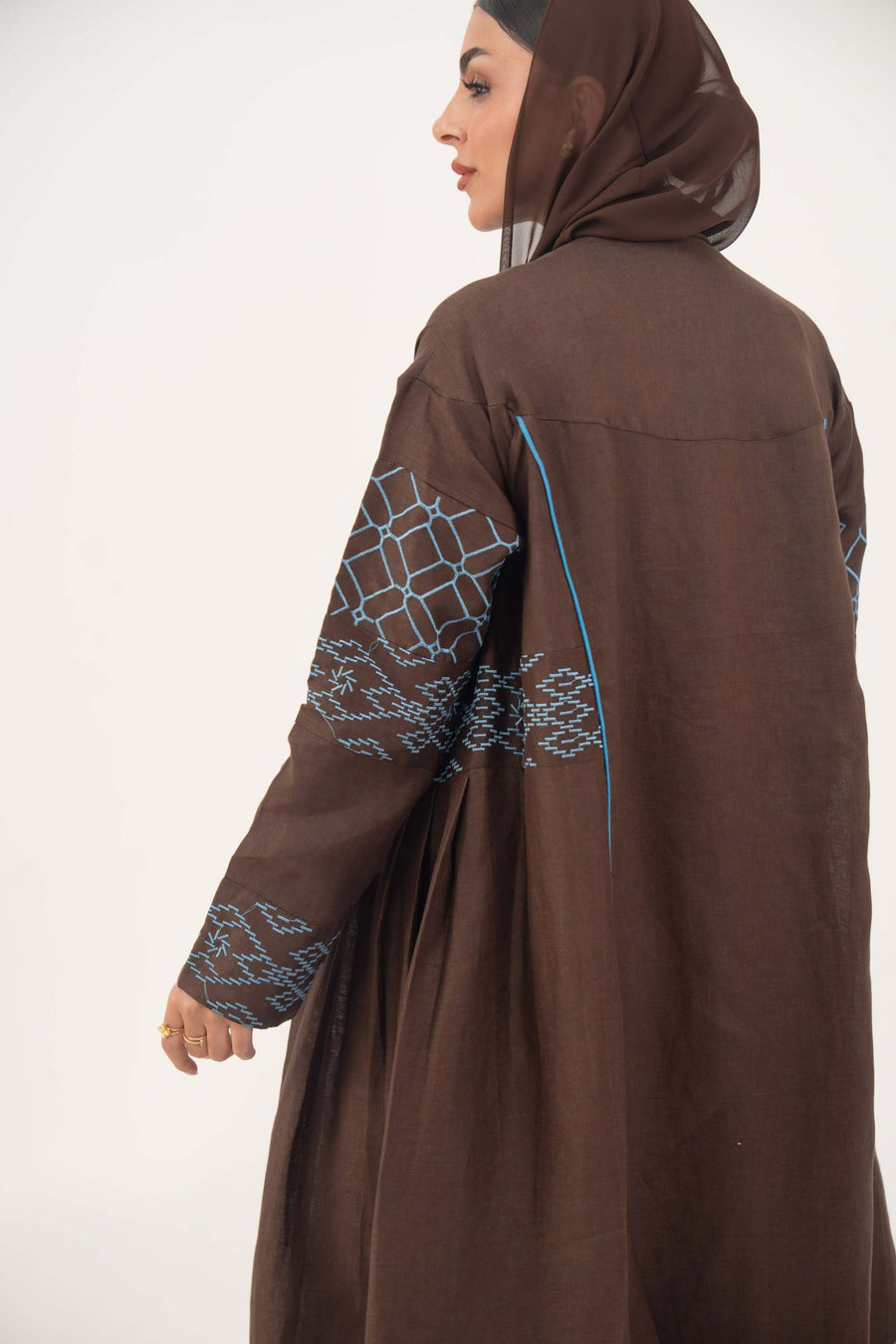 Mocha brown linen-blend abaya with sky-blue embroidery and batwing sleeves featuring blue piping and light-blue cuff details.