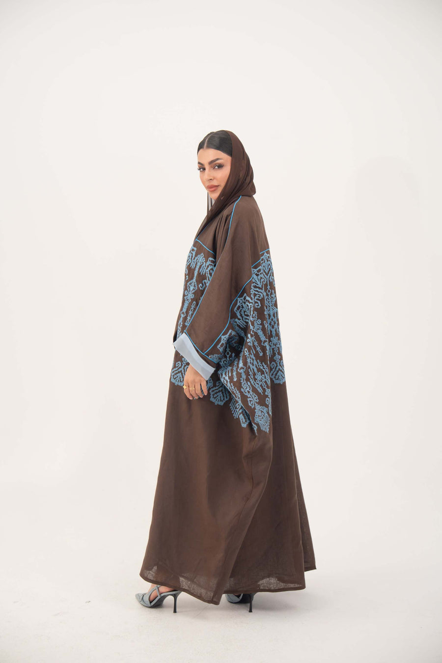 Brown Bisht abaya with intricate blue embroidery and rolled cuffs on wide sleeves.
