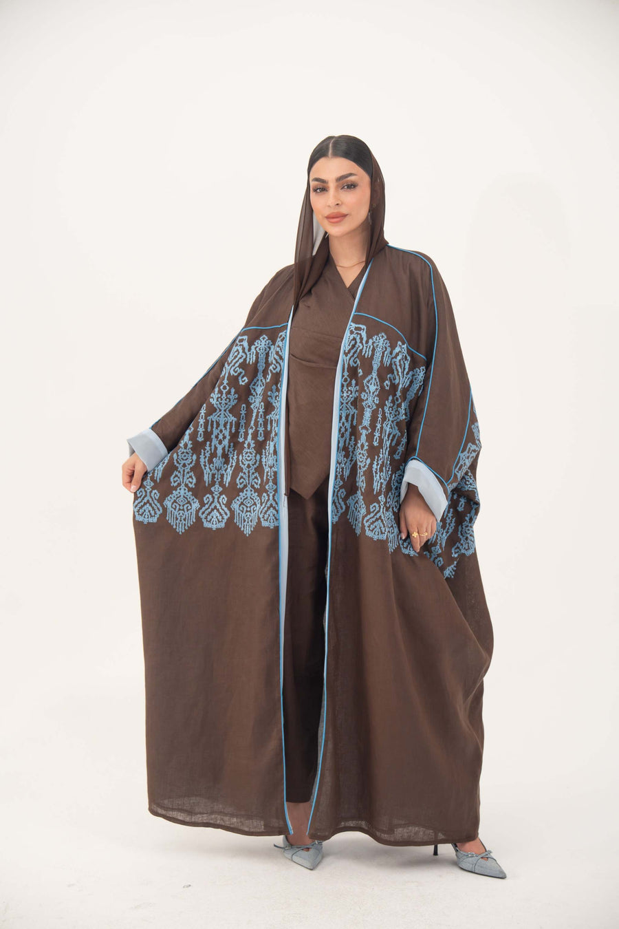 Mocha brown Zyra bisht abaya with blue shak embroidery, light blue piping, rolled cuffs, and flowy batwing linen design.