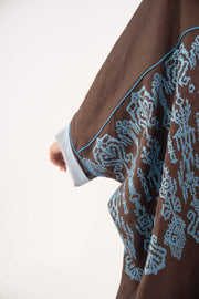 Close-up of mocha brown linen bisht abaya with blue shak embroidery and light blue piping on sleeves and cuffs.
