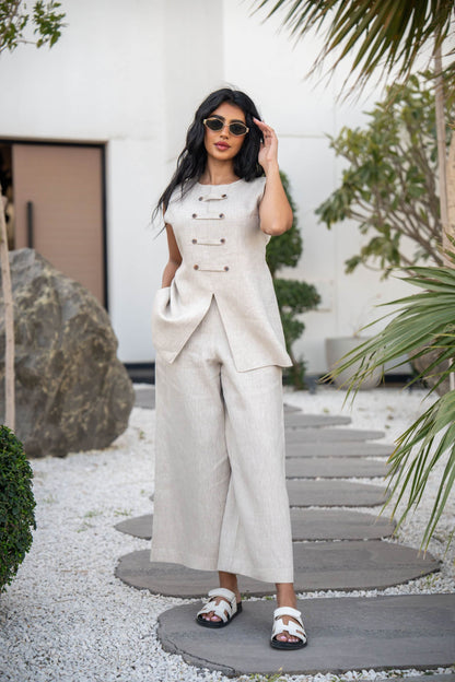 Woman wearing beige sleeveless linen vest with double-breasted buttons and matching wide-leg linen pants outdoors