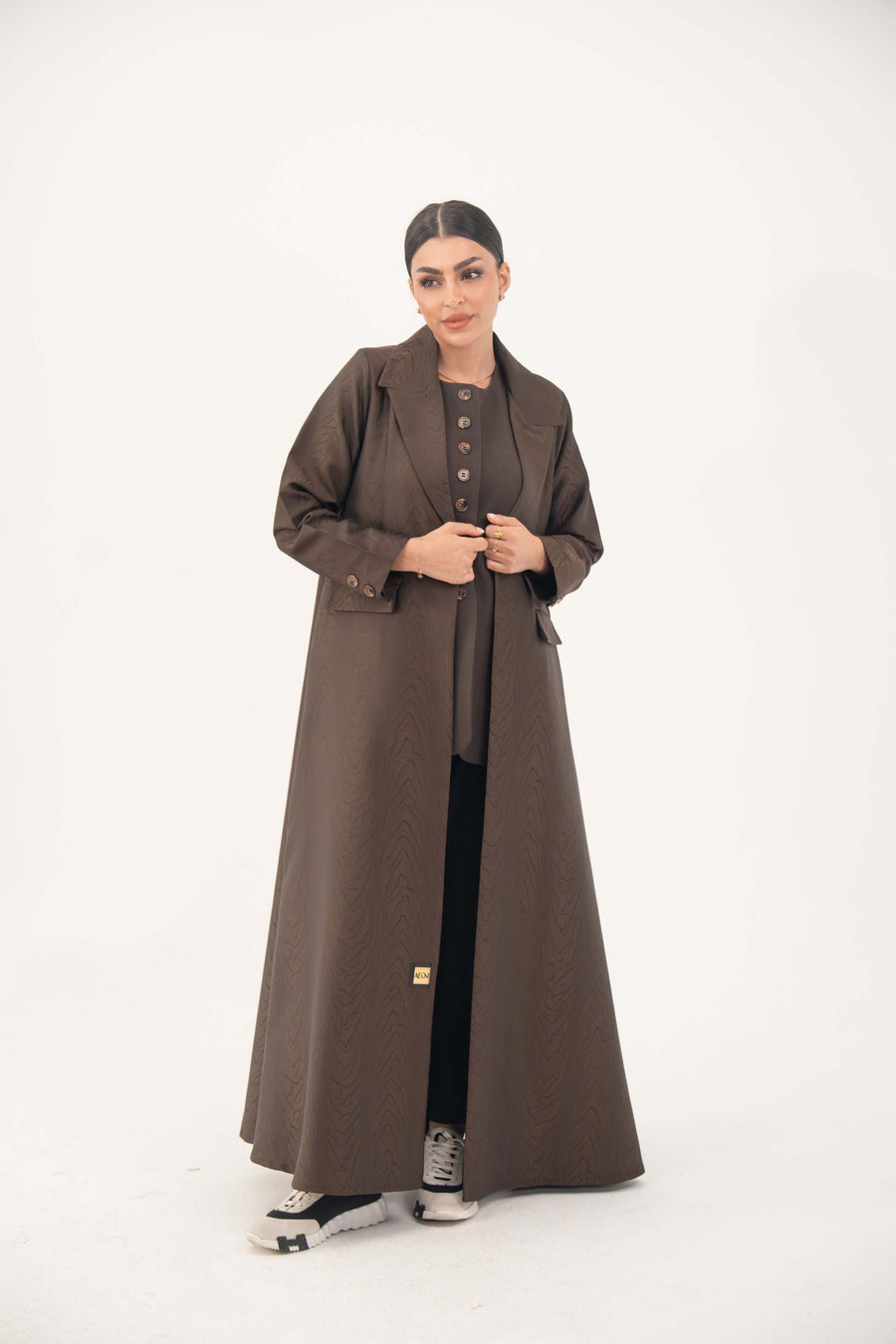 Woman wearing a brown jacquard blazer abaya with sharp lapels, structured tailoring, and faux pockets, styled for formal and professional looks.