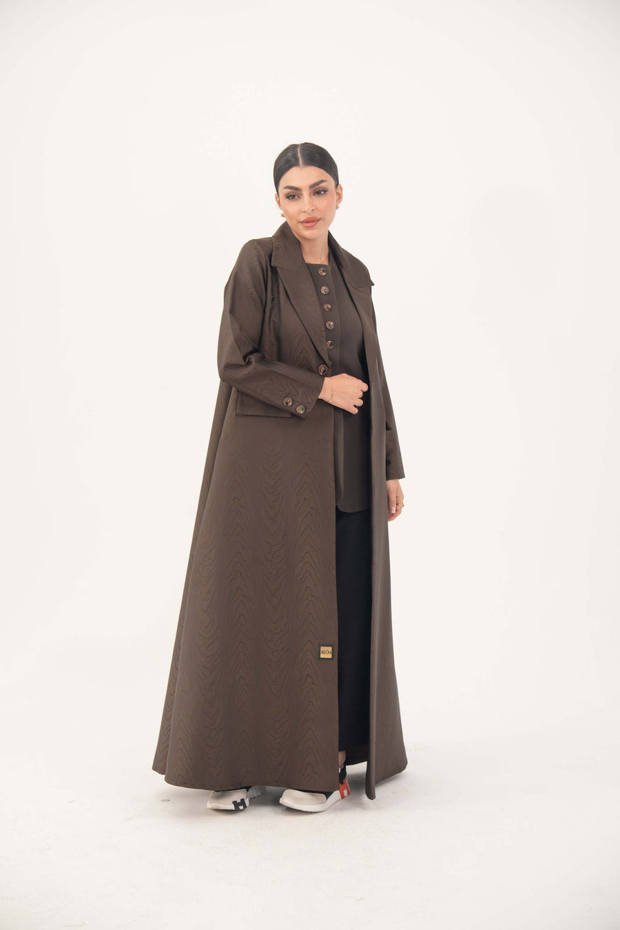 Woman wearing a dark chocolate brown jacquard blazer abaya with sharp lapels, structured tailoring, and faux pockets.