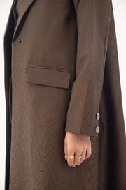 Close-up of brown jacquard blazer abaya with sharp lapels, faux pockets, and two buttons on the sleeve, showcasing textured fabric and tailored design.