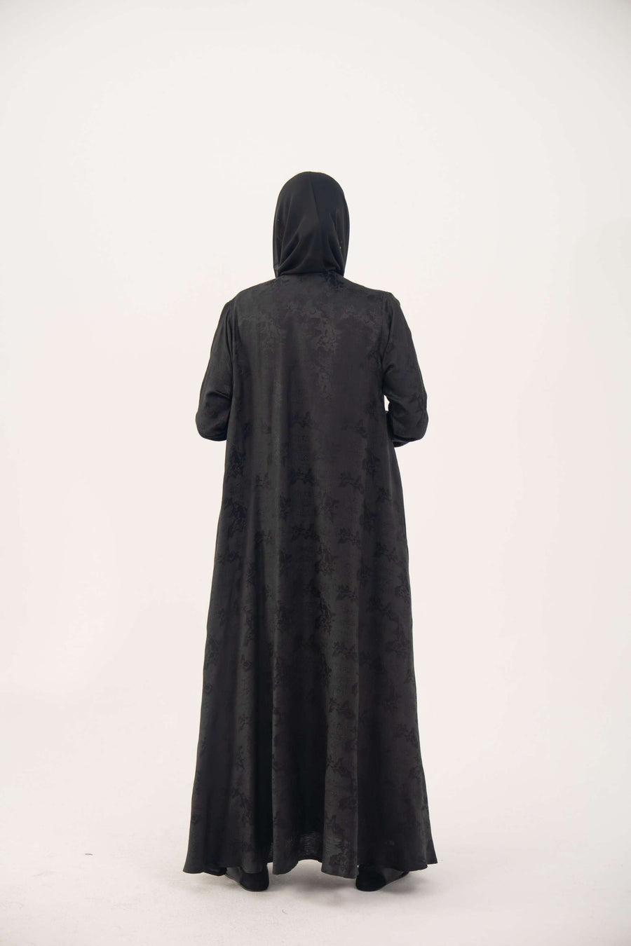 Back view of a black jacquard silk abaya with tone-on-tone floral weave, featuring a fluid A-line cut, relaxed shoulders, open front, straight sleeves, and discreet side pockets.