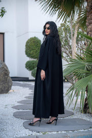 Woman wearing a classic black crepe abaya with a flowing silhouette and button-down front outdoors - Hannah