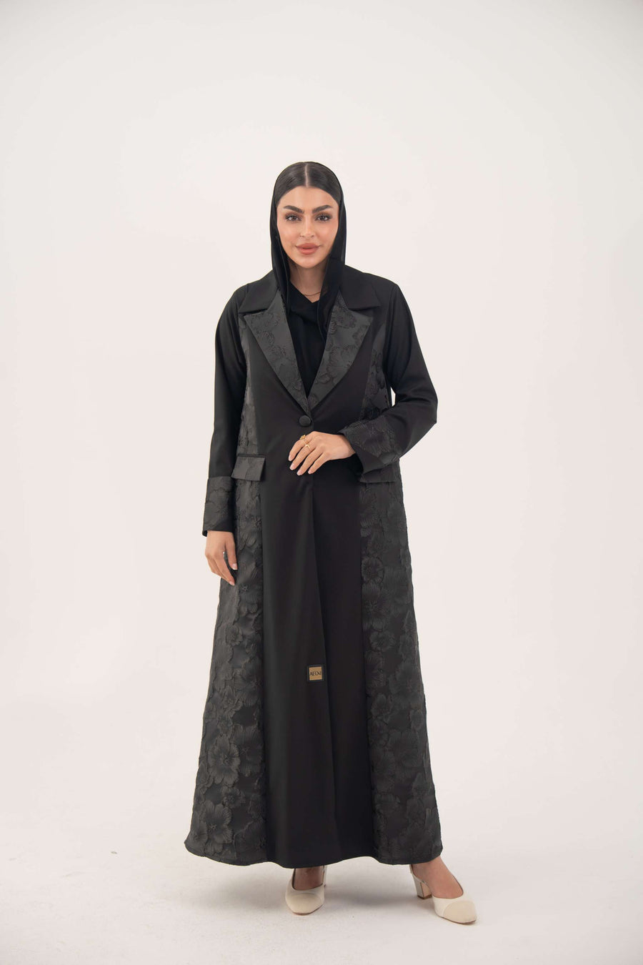 Woman wearing a black jacquard blazer abaya with a textured pattern and classic lapels, featuring a tailored and elegant silhouette.