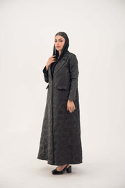 woman wearing elegant black jacquard blazer abaya with textured pattern and classic lapels standing against white background