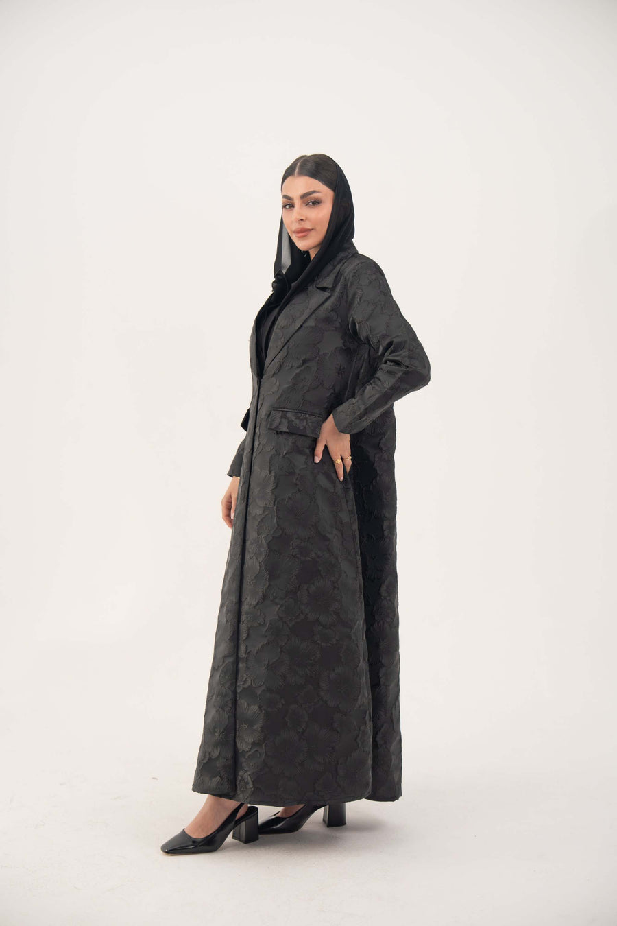 Woman wearing a black jacquard blazer abaya with textured pattern and classic lapels, styled for formal occasions.