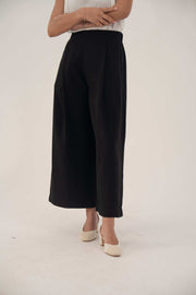 Classic black wide-leg crepe pants with soft front pleats and elastic back, cropped at ankle for layering.