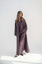 Woman wearing tailored blazer abaya in soft neutral tone with structured lapels, statement buttons, side flap pockets, and hidden inner pockets.
