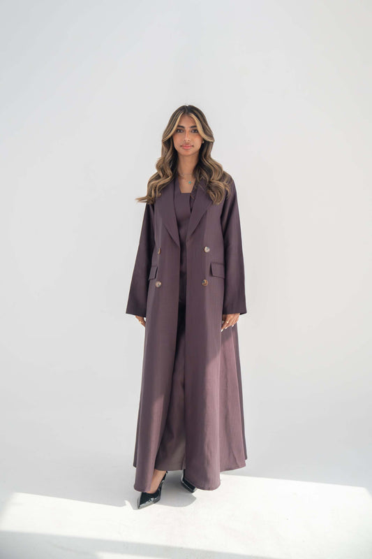 woman wearing ube-colored tailored blazer abaya with sharp lapels and statement buttons standing against white background