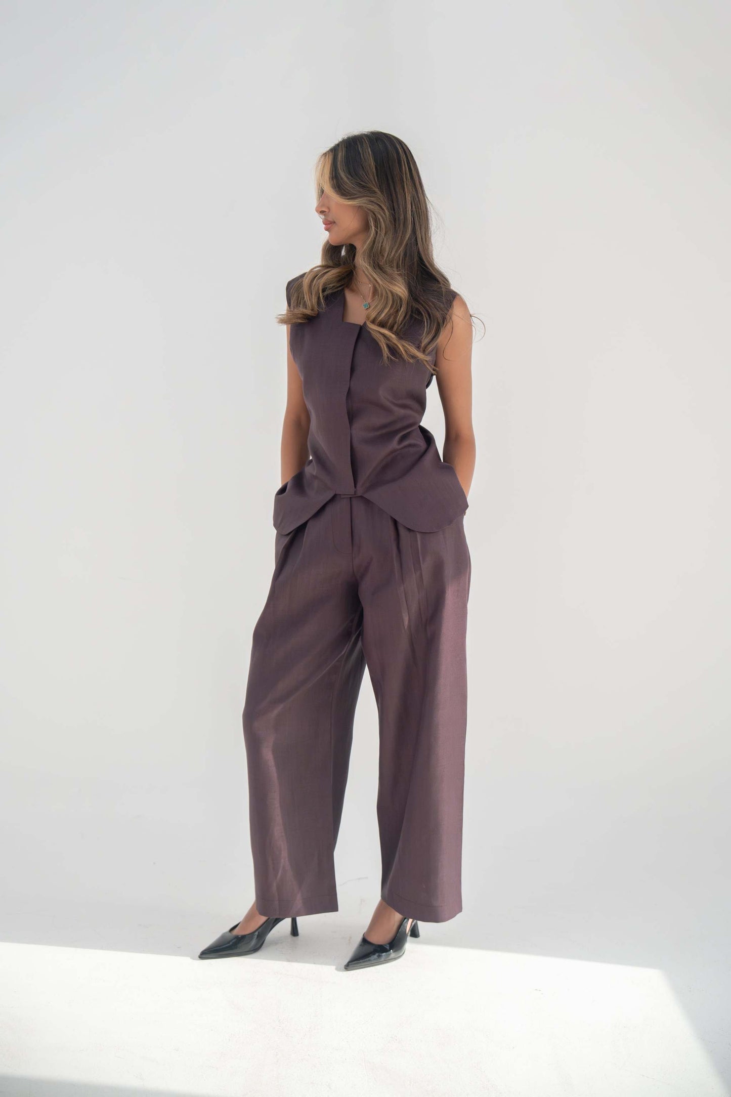 Woman wearing high-waisted relaxed fit ube pant in purplish brown twill linen blend with straight legs and black heels.