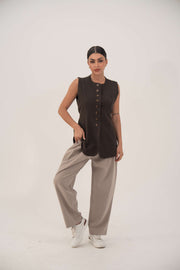 Woman wearing beige Truffle Crepe Pants with a black sleeveless buttoned top and white sneakers, posing against a plain background.