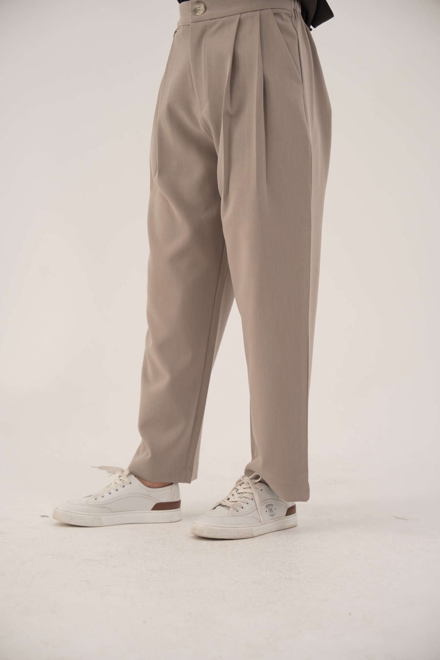 Beige Truffle Crepe Pant with high waist and subtle front pleats, styled with white sneakers.