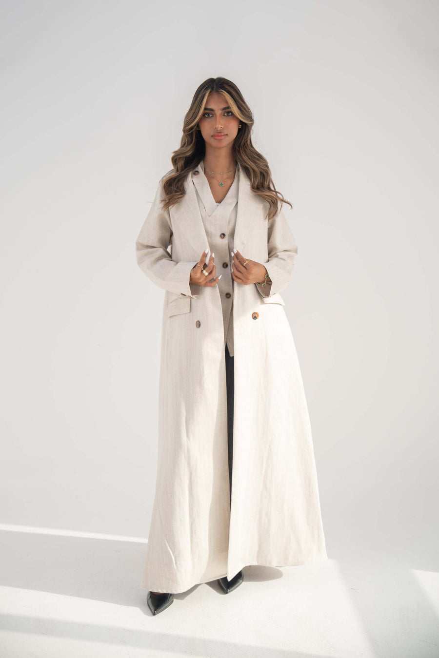Woman wearing a warm beige blazer-style abaya with notched lapel and front buttons, featuring flap and hidden pockets, styled for everyday elegance.