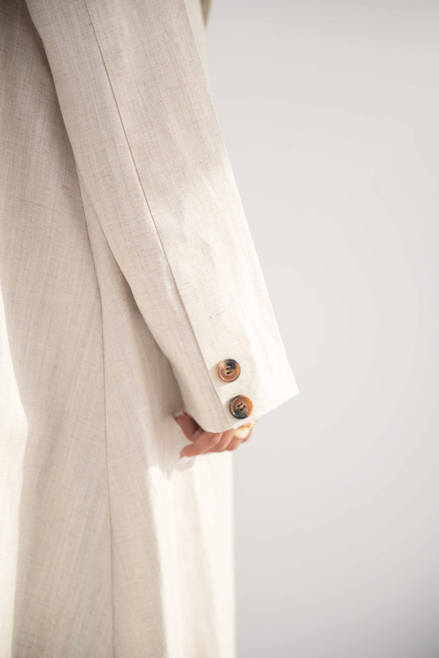 Close-up of beige twill linen blend blazer-style abaya sleeve with two buttons on cuff and soft flowing fabric.