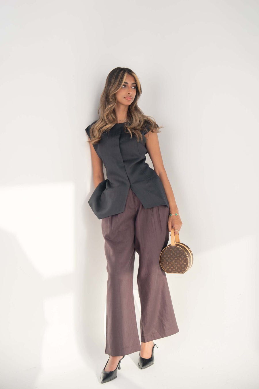 woman wearing navy Blueberry Blouse with structured cut and hidden front buttons paired with wide-leg pants and black heels holding a round handbag against white background