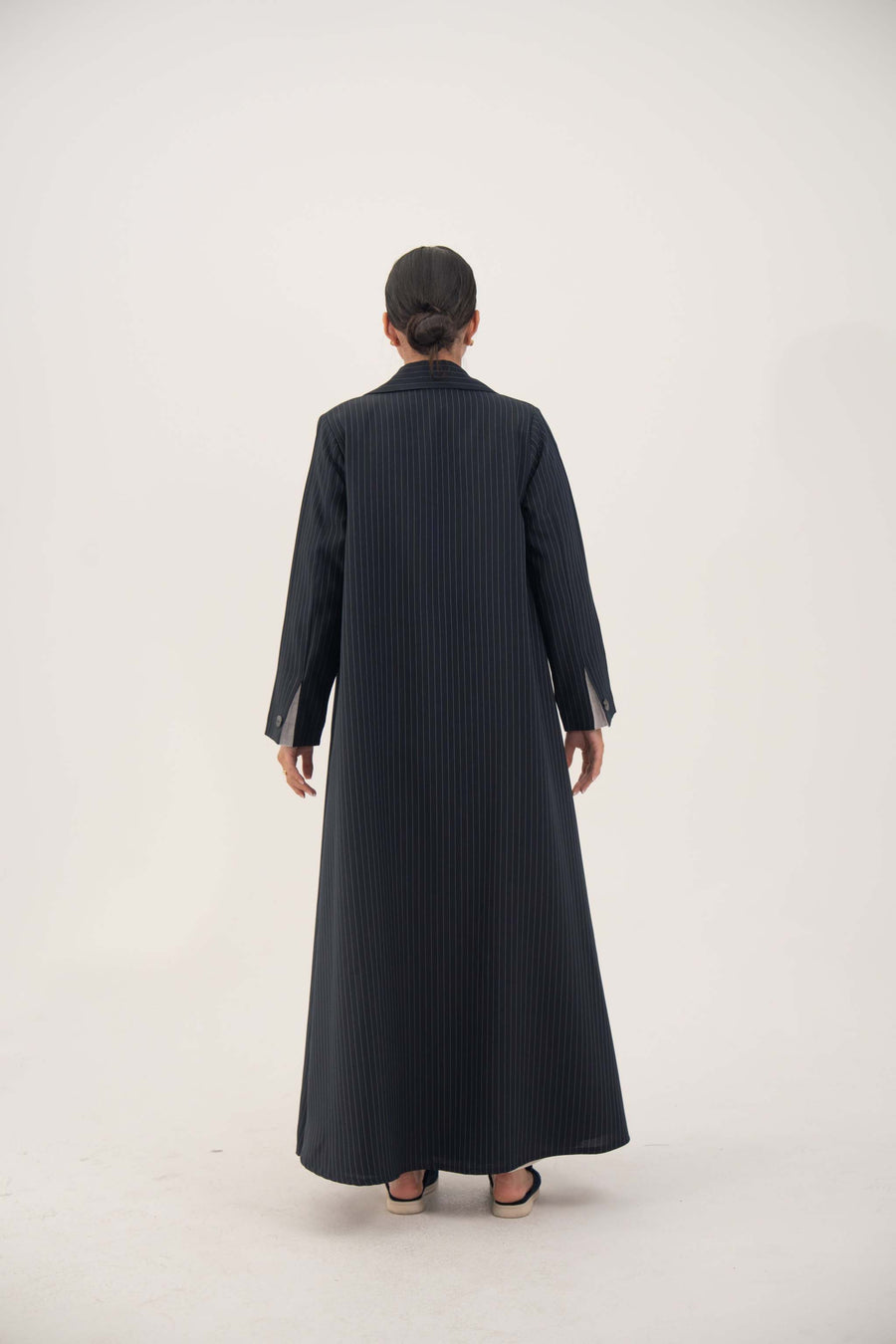 Back view of a Zanira premium crepe blend open-front blazer abaya in deep navy with fine white pinstripes, featuring wide lapels, shoulder pads, decorative pockets, inner pocket, and buttoned cuff straight sleeves.