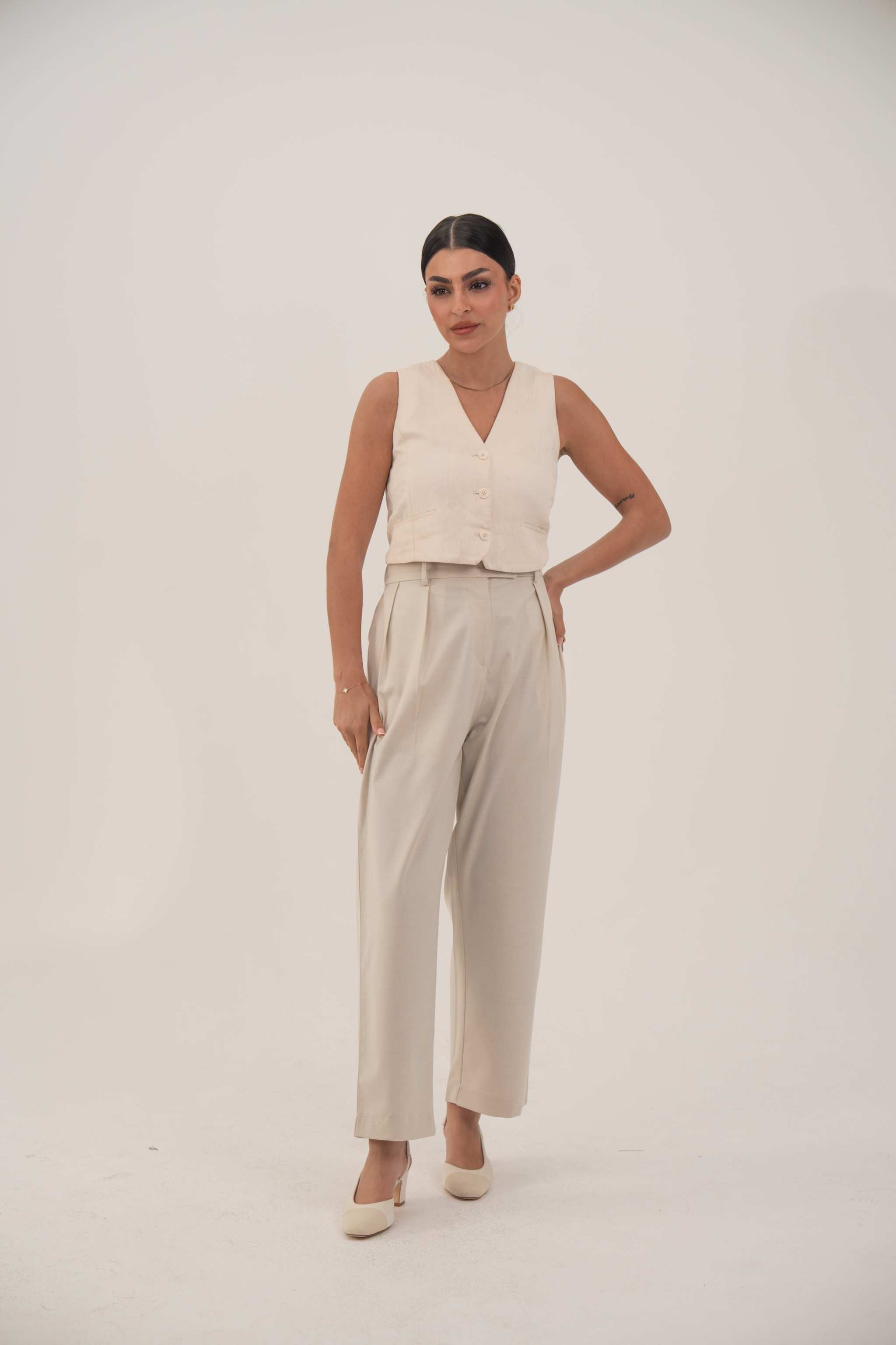 Woman wearing soft beige sleeveless crepe vest with front buttons and light beige pants