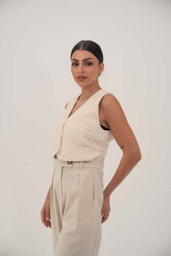 Woman wearing a sleeveless beige crepe vest with front buttons and matching high-waisted beige pants against a plain background