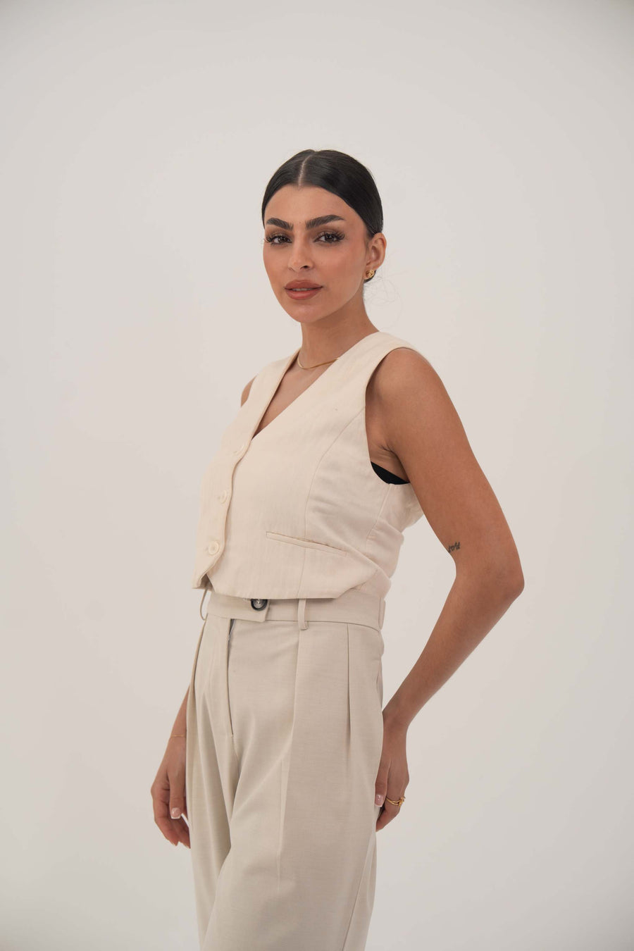 Woman wearing a beige sleeveless crepe vest with front buttons and matching high-waisted trousers