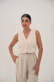 Woman wearing a soft beige sleeveless crepe vest with front button closure and light beige pants.