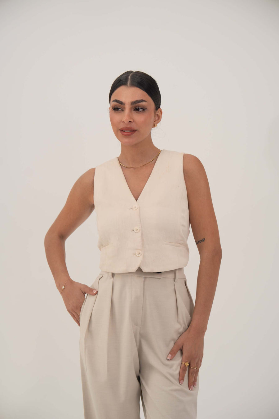 Woman wearing a soft beige sleeveless crepe vest with front button closure and light beige pants.