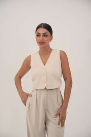 Woman wearing a beige sleeveless crepe vest with front buttons and high-waisted beige pants