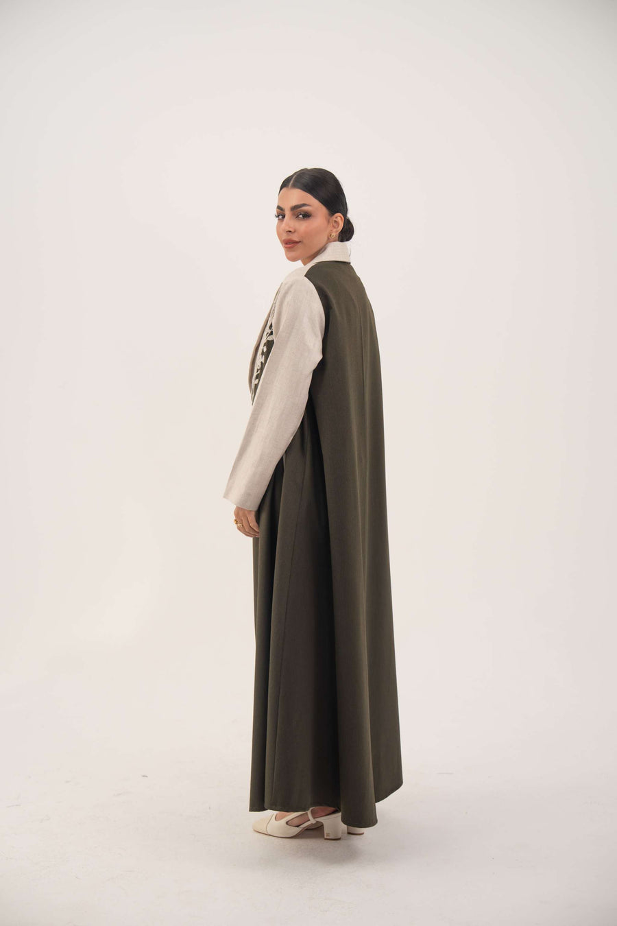 Elegant deep olive green abaya with beige linen panels, white leaf embroidery, notched lapels, full-length cut, and side slit pockets.