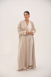 Woman wearing a beige airy premium linen abaya with tonal embroidery and soft chiffon cuffs, styled in a classic bisht silhouette.