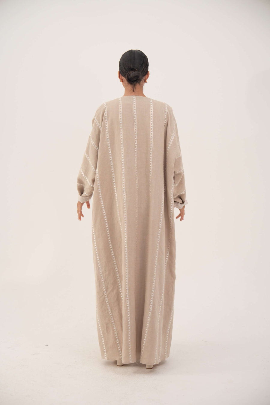 Back view of a creamy beige airy linen abaya with subtle tonal embroidery and soft chiffon cuffs, featuring a classic bisht silhouette and open front for graceful flow.