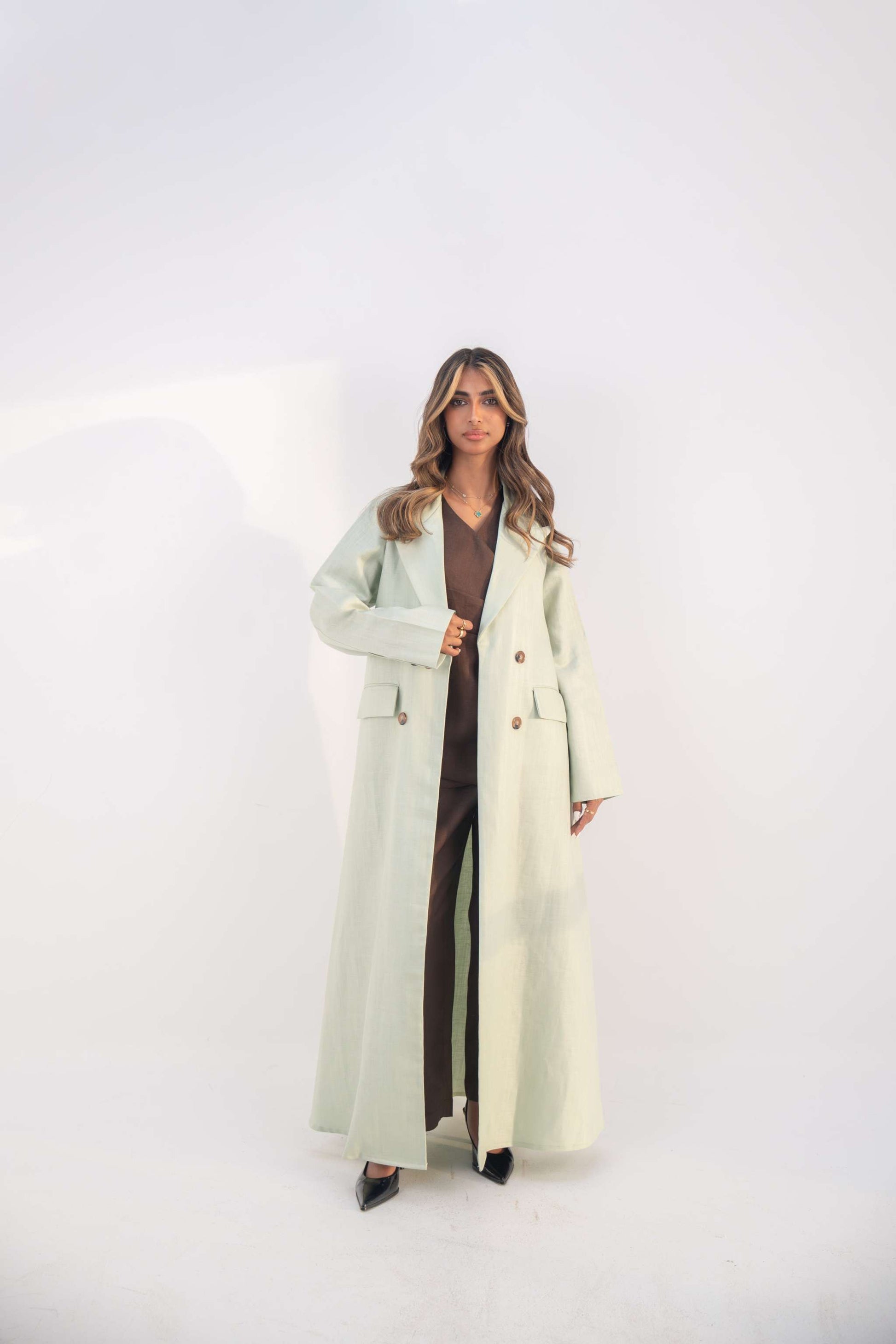 woman wearing mint green blazer abaya with structured lapels and statement buttons standing against white background