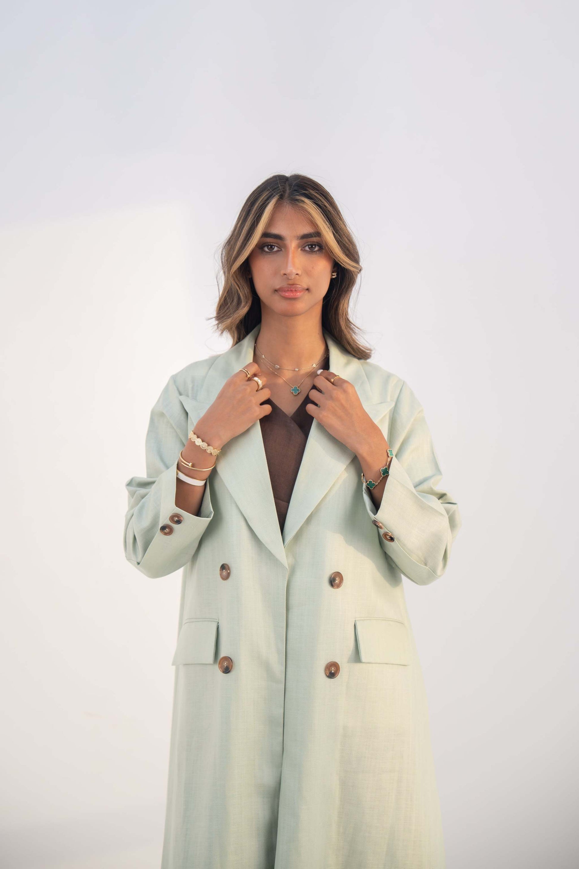 Woman wearing a mint green tailored blazer abaya with structured lapels and statement buttons.