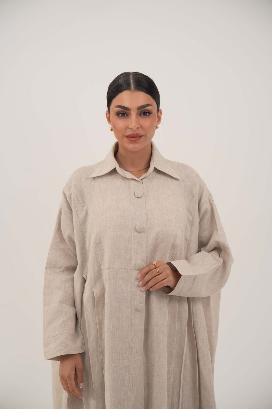 Sandora soft beige linen abaya with shirt collar and fabric-covered buttons, featuring fine pleats from shoulders to hem.