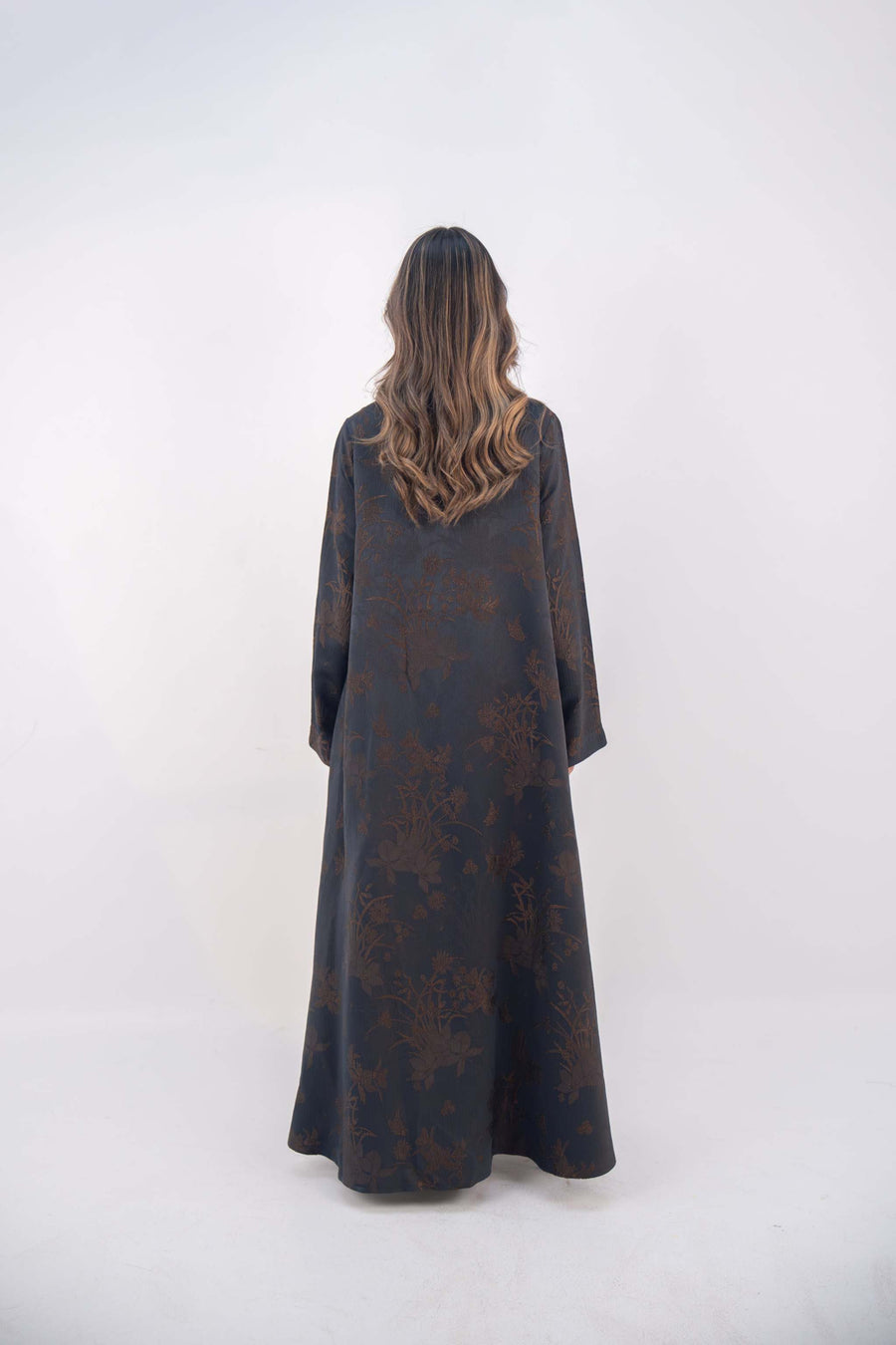Back view of a navy jacquard silk abaya with subtle brown floral patterns and wide sleeves on a standing woman